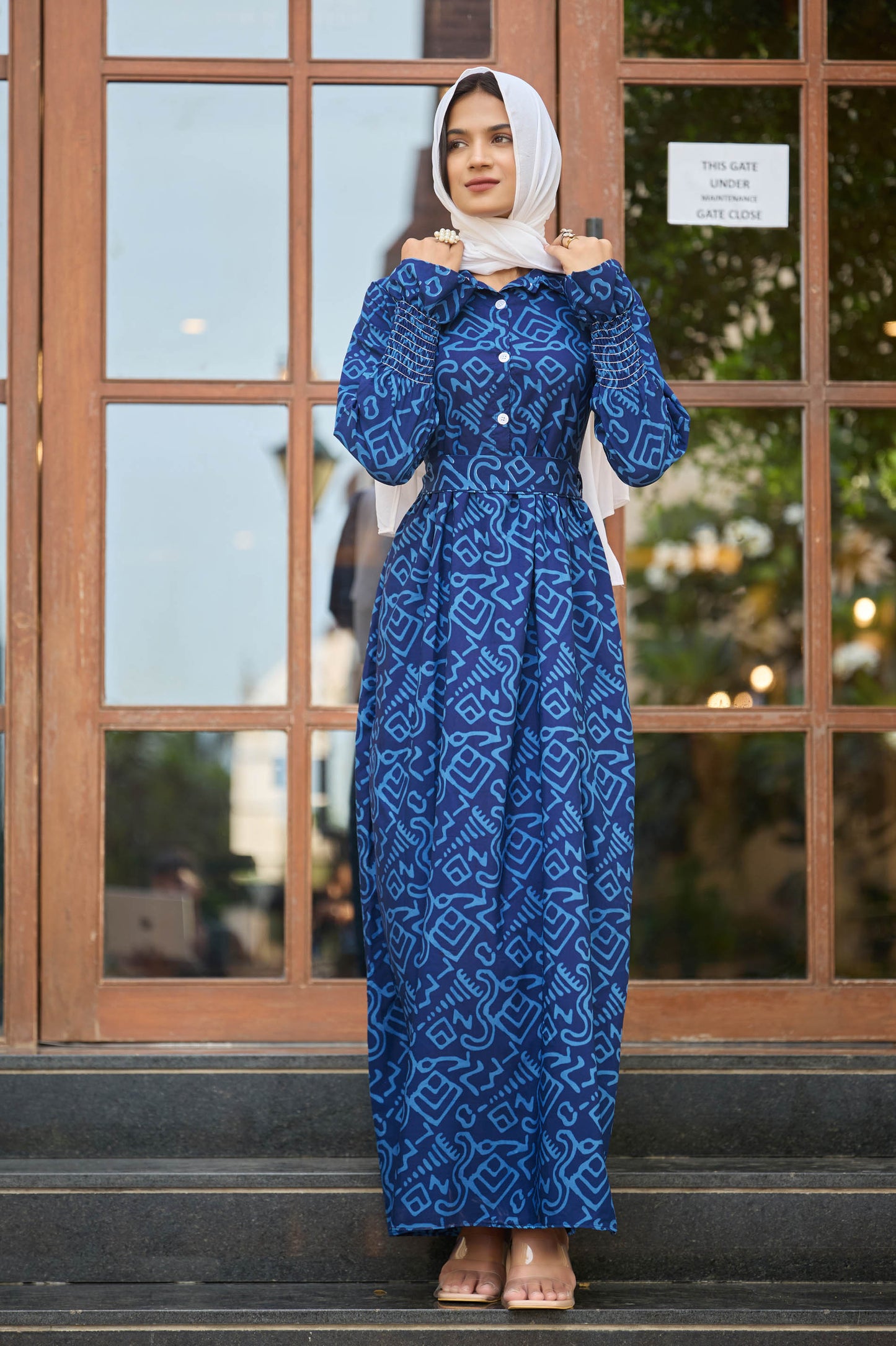 Woman wearing a blue patterned dress standing in front of a glass door.