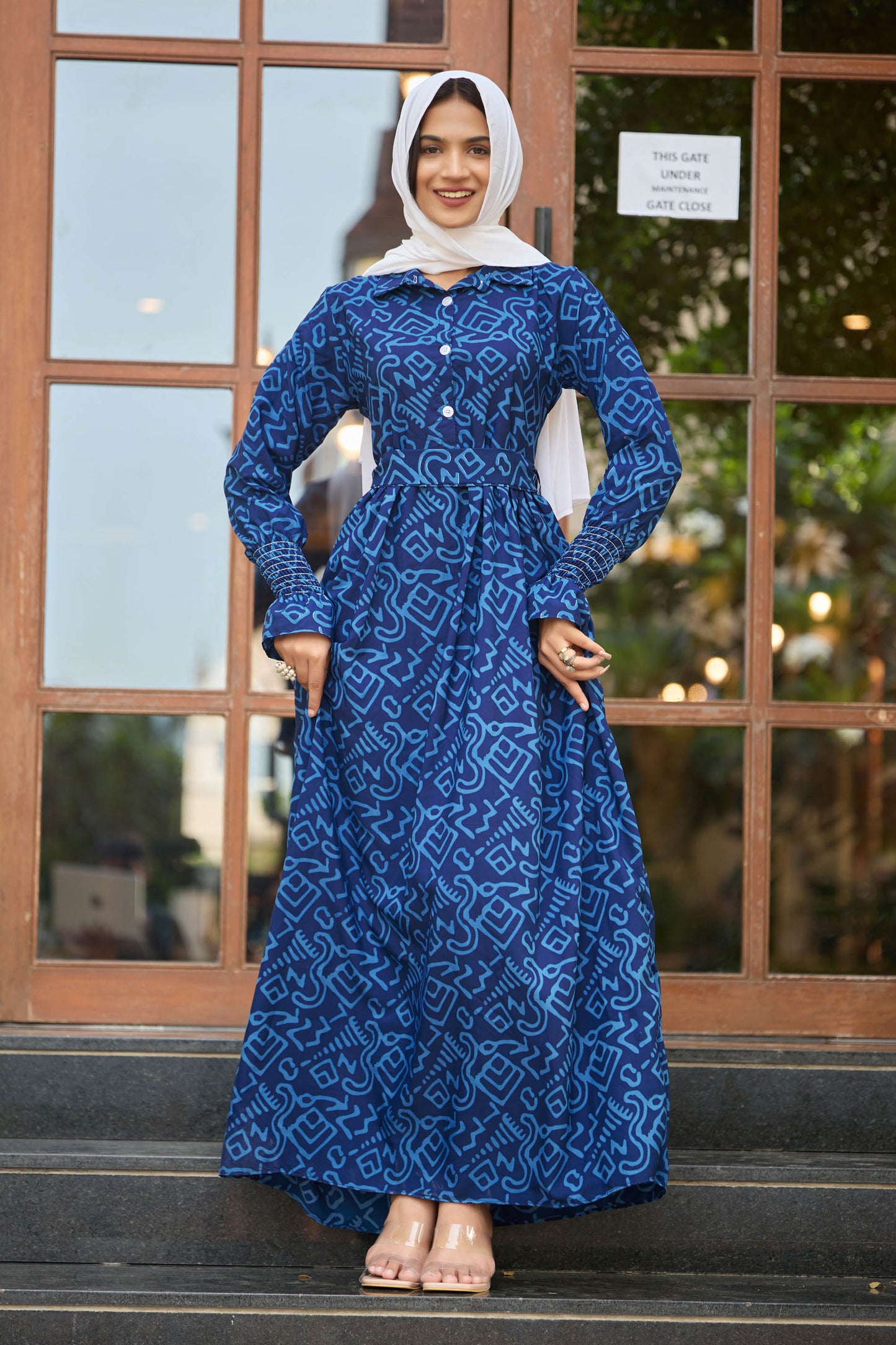 Woman wearing a blue patterned dress standing in front of a glass door.